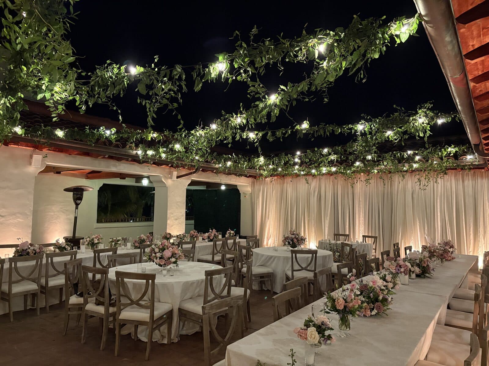 Blush and lavender floral centerpieces beneath greenery-and-string-light garlands