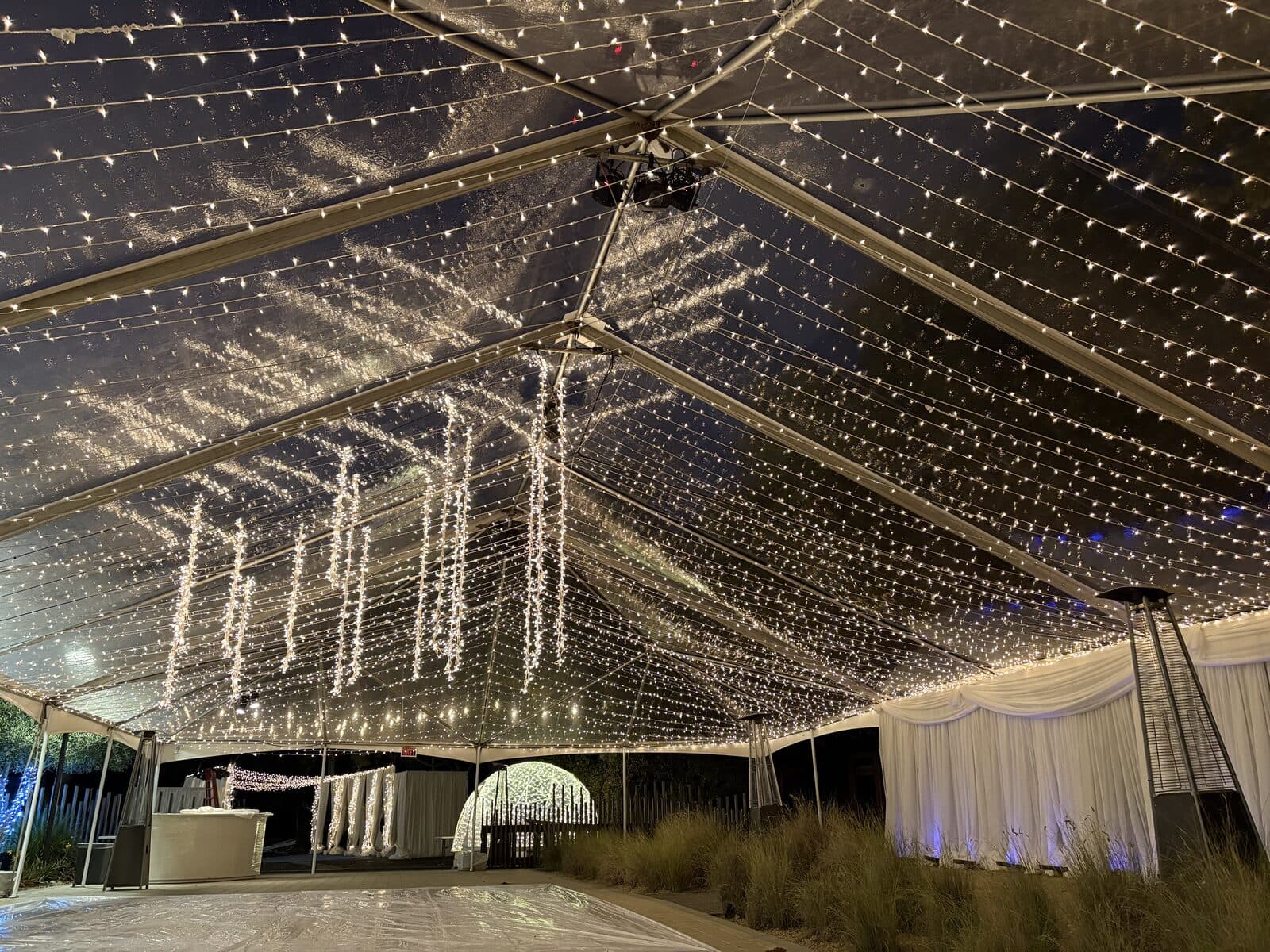 A clear-top tent ceiling filled with thousands of warm string lights
